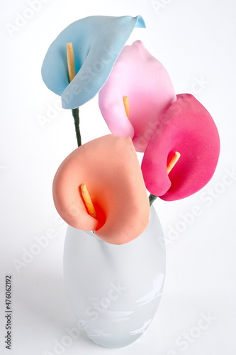 Four pastel colored foam lilies in a frosted glass vase against a white background. photo