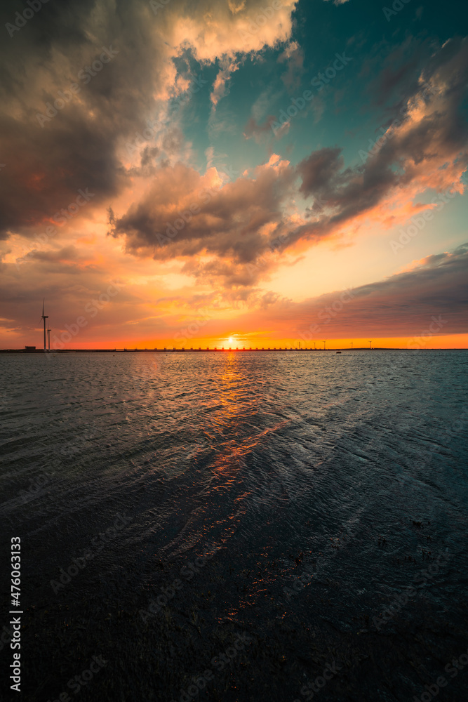 Vertical shot of the beautiful sunset above the sea. Oosterscheldekering, the Netherlands. - obrazy, fototapety, plakaty 