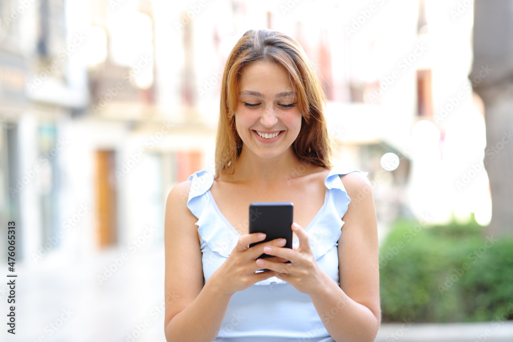 Happy female walking using smartphone in the street
