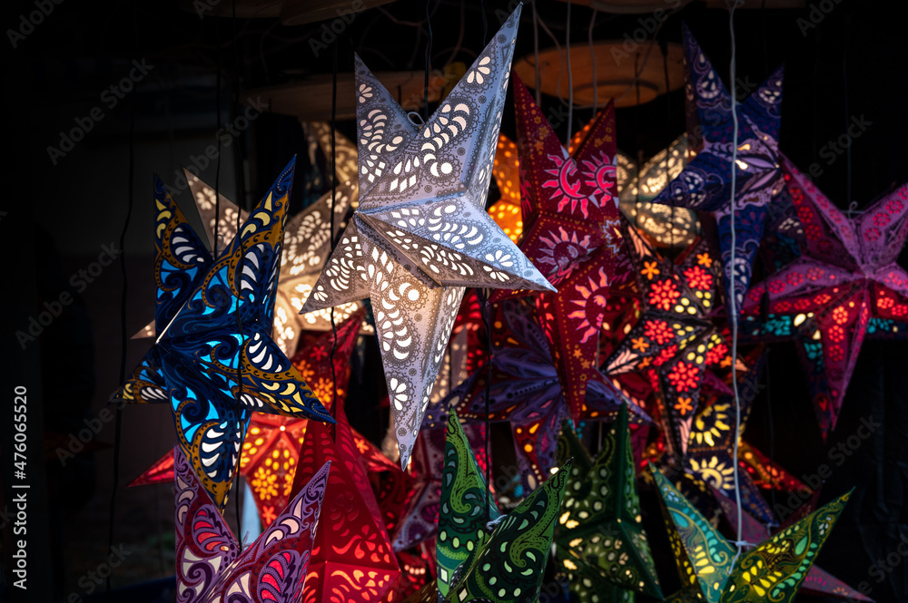 Shining Christmas stars folded from paper in different colors in a market stall, lantern for the dark winter holidays, copy space, selected focus