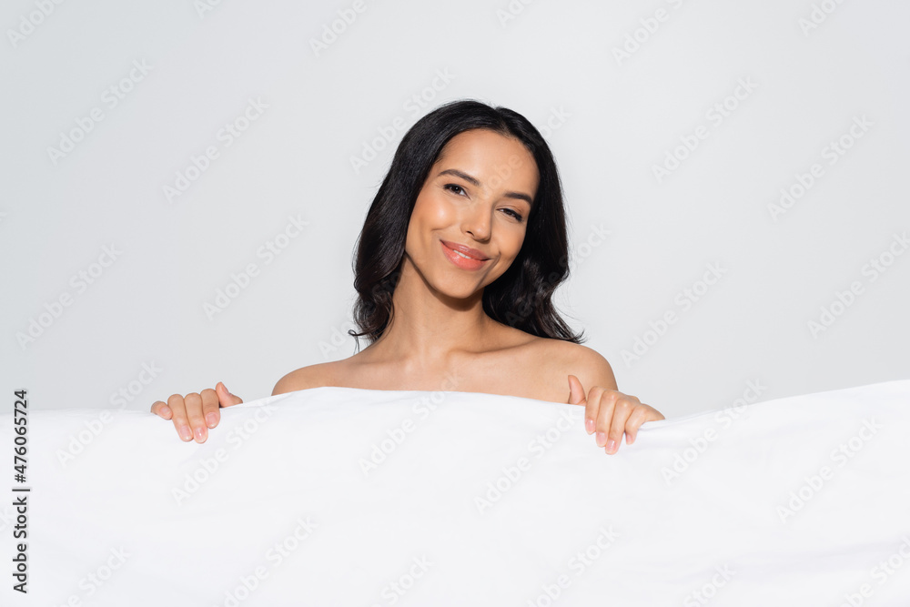 brunette woman smiling at camera while posing behind white blanket isolated on grey. brunette woman smiling at camera while posing behind white blanket isolated on grey.