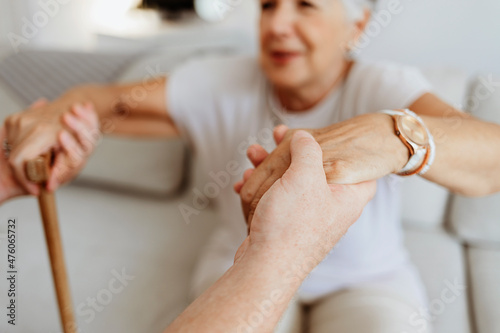 Cropped shot a young male home carer supporting old woman to stand up from the sofa at care home. Photo of male professional caregiver taking care of elderly woman at home during the day. photo