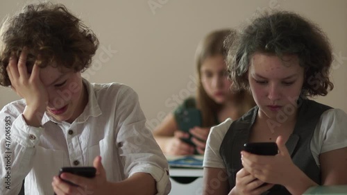 Children and gadgets. School students at school are busy with their smartphones. A boy and a girl are sitting at a desk and looking at screens from their phones