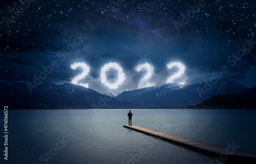 Obraz na plátně New year 2022 at night, man standing on a wooden dock on a lake and looking to t