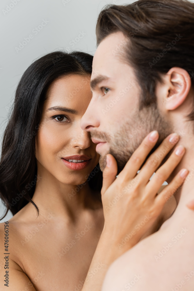 young passionate woman looking at camera while touching face of young man isolated on grey. young passionate woman looking at camera while touching face of young man isolated on grey.