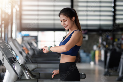 Beautiful young Asian woman preparing to set up watch before running in machine treadmill at fitness gym club.