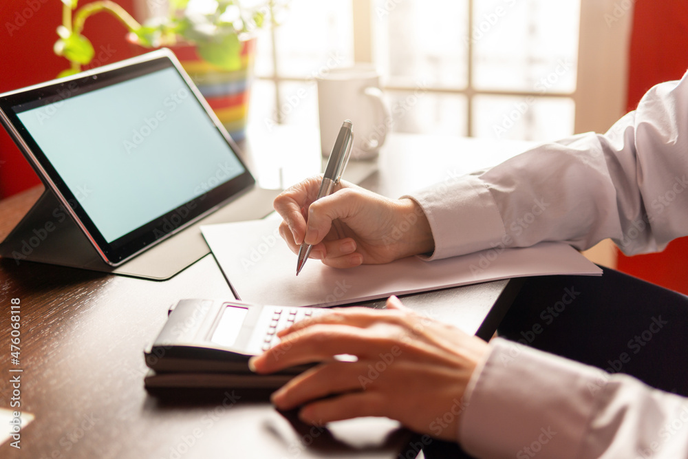 Fototapeta premium Woman writing and using a calculator, using digital tablet, businesswoman or student. Working from home concept