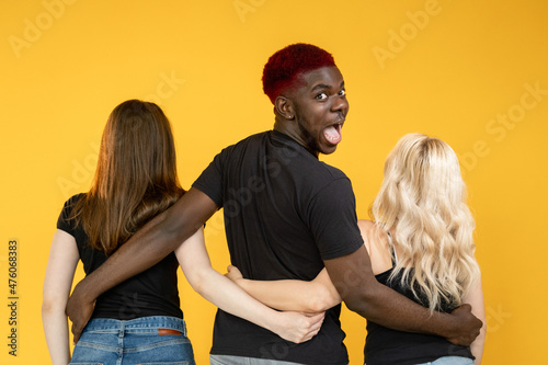 Open relationship. Casanova man. Multiracial love. Date luck. Lovelace successful amazed happy  guy embracing two different women together isolated on orange background. photo