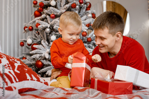 Portrait of cheerful father and son opening a Christmas gift in the bedroom near the New Year tree