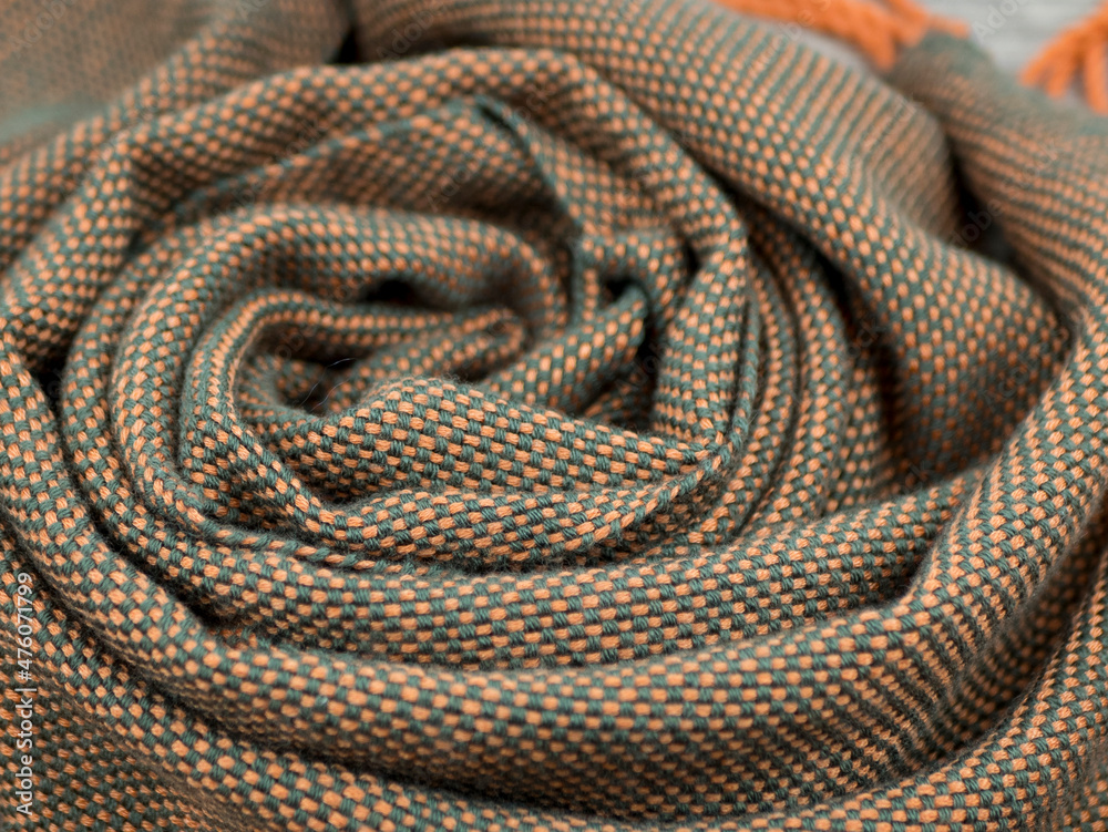 Fototapeta premium The interwoven of green and orange threads of the handmade fabric. Draped woolen shawl or plaidy, close up