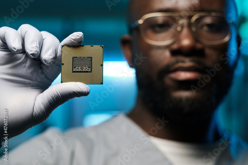 Gloved hand of contemporary technician of African ethnicity showing microchip while holding it in front of camera photo
