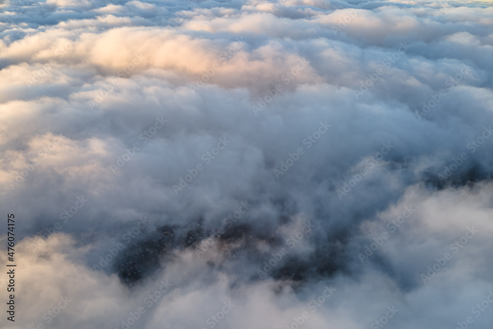 Aerial view from high altitude of distant city covered with puffy cumulus clouds flying by before rainstorm. Airplane point of view of landscape in cloudy weather