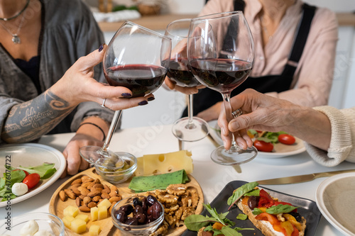 Close-up of women toasting with glasses of red wine while sitting at dining table with appetizers