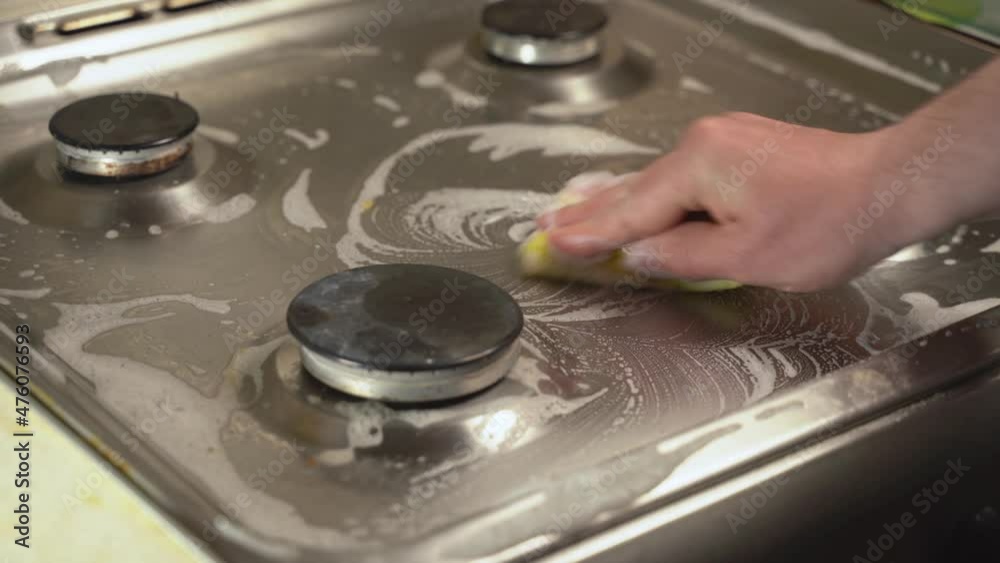 Man washing gas stove with yellow sponge, hand close-up Man washing gas stove with yellow sponge, hand close-up