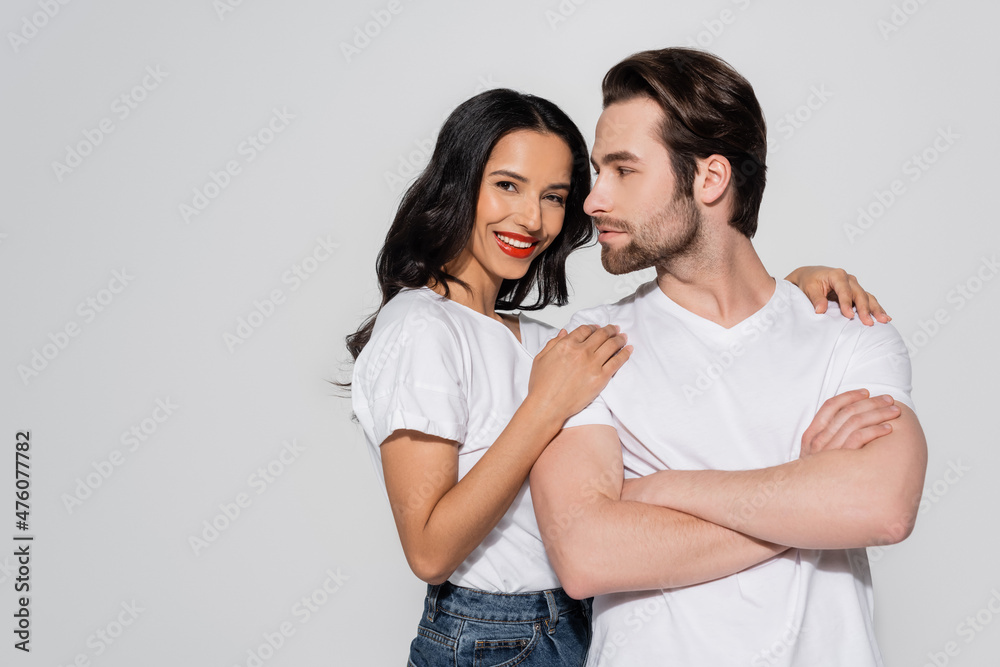 smiling brunette woman looking at camera while hugging shoulders of man standing with crossed arms isolated on grey. smiling brunette woman looking at camera while hugging shoulders of man standing with crossed arms isolated on grey.
