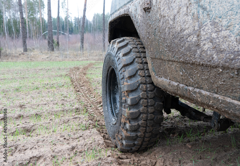 Fototapeta premium Photo of an off-road black car on muddy gravel road. Rally racing SUV in the forest with trees. Automobile wheel with tire