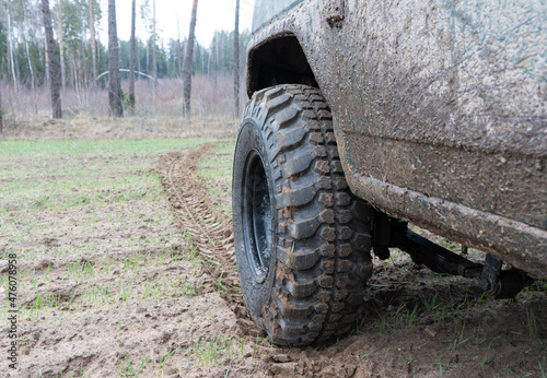 Photo of an off-road black car on muddy gravel road. Rally racing SUV in the forest with trees. Automobile wheel with tire