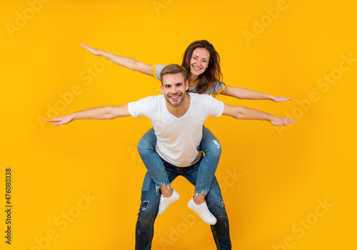 Happy playful woman and man pretend flying doing piggyback ride yellow background, fun photo