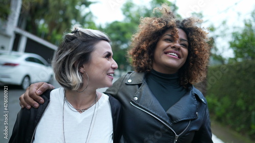 Two happy women diverse friends walk together in urban street