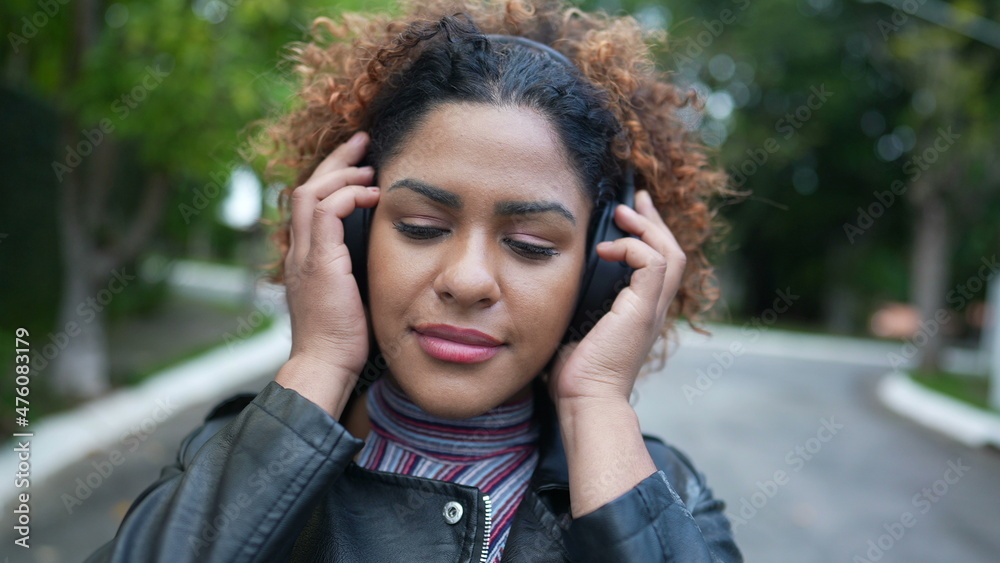 Brazilian woman putting headphones over the ear outside listening to music or podcast Brazilian woman putting headphones over the ear outside listening to music or podcast