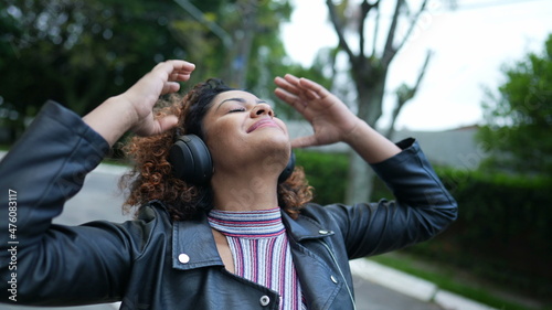 Carefree black woman dancing to music outside in street wearing headphones