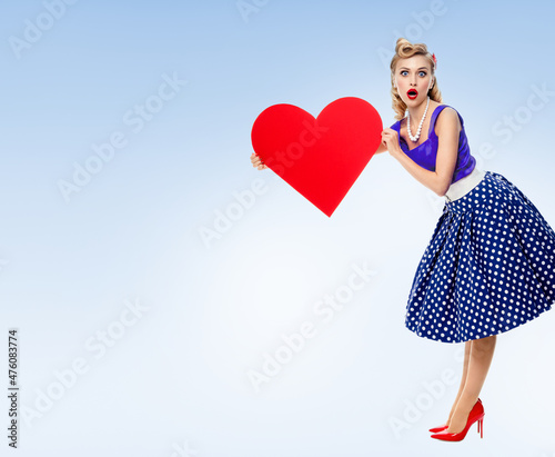 Obraz na płótnie Full body of woman holding heart symbol, dressed in pin-up style dress with polka dot, over light blue background