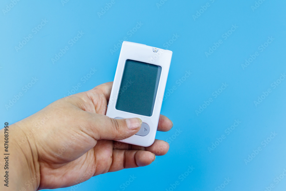 Digital glucometer in female hand over a pastel blue background. Diabetes concept Digital glucometer in female hand over a pastel blue background. Diabetes concept