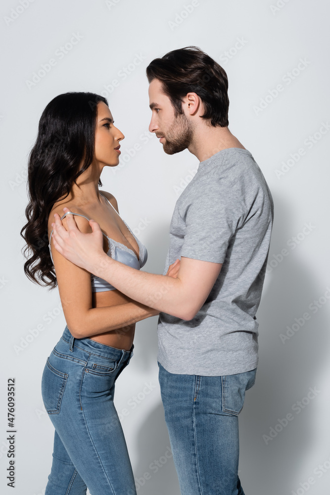 side view of brunette woman in bra embracing man in t-shirt on grey. side view of brunette woman in bra embracing man in t-shirt on grey.