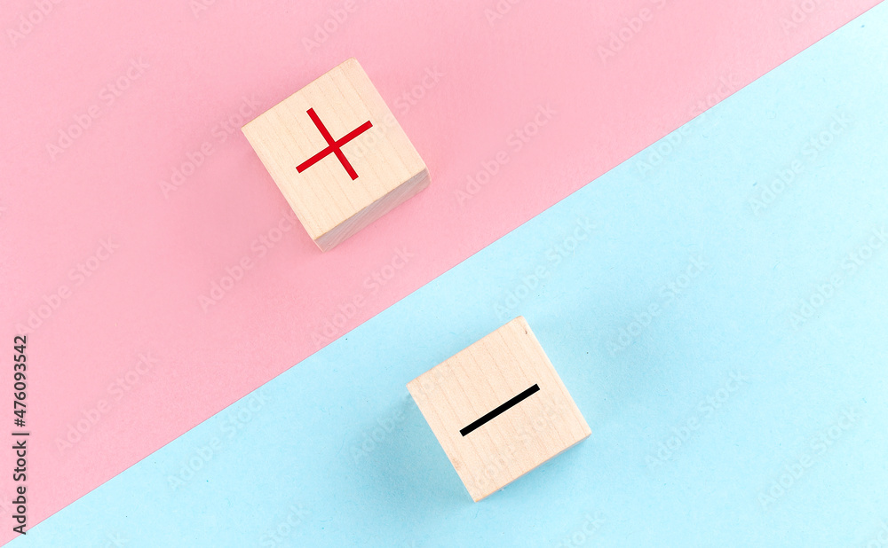 PLUS and MINUS symbols on wooden block on the pink and blue background PLUS and MINUS symbols on wooden block on the pink and blue background