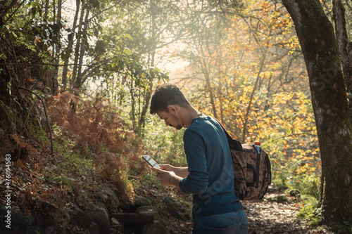 young man on a walk in the forest in autumn, sits down on a stone and looks at his cellphone