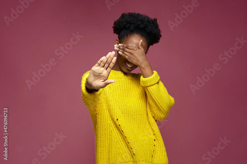 Embarrassed shy young african american girl cover eyes with hand, do stop gesture, smiling, refuse to look at something 