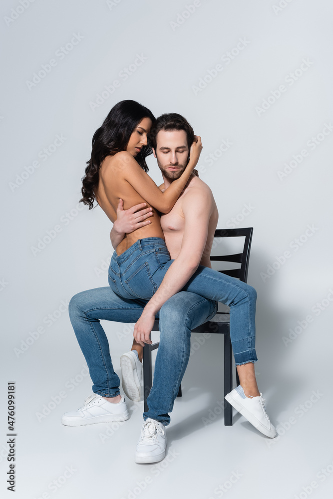 shirtless man in jeans sitting on chair with passionate girlfriend on grey. shirtless man in jeans sitting on chair with passionate girlfriend on grey.