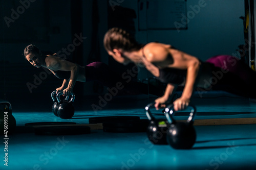 A young woman in a gym doing push-ups with the help a kettlebell weight