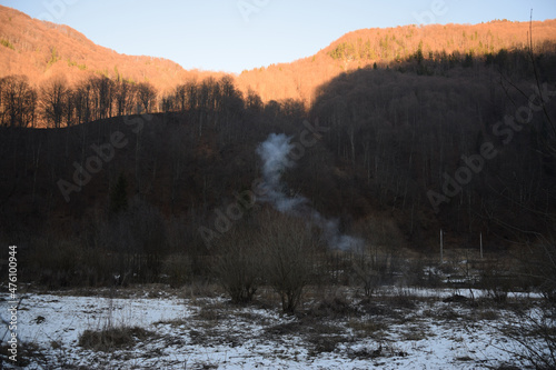 Mountain forest with snow melting on the ground against forest trees with sunlit photo