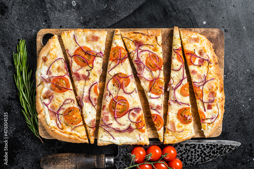 Homemade Flammkuchen or tarte flambee with cream cheese, bacon, tomato and onions. Black background. Top view