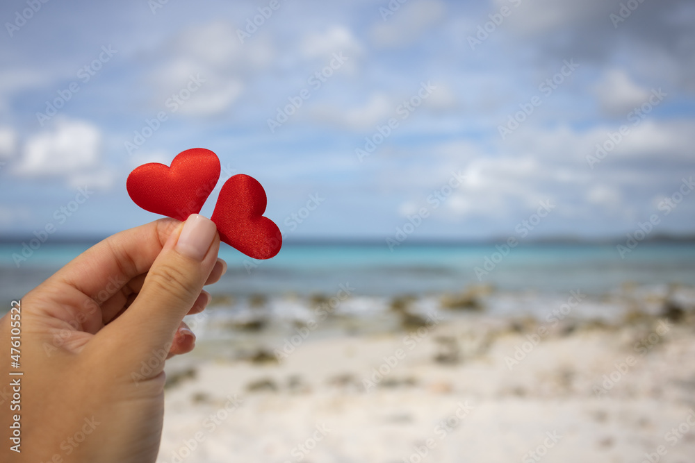 Female hand holding two small hearts on the background of the seascape. Female hand holding two small hearts on the background of the seascape.
