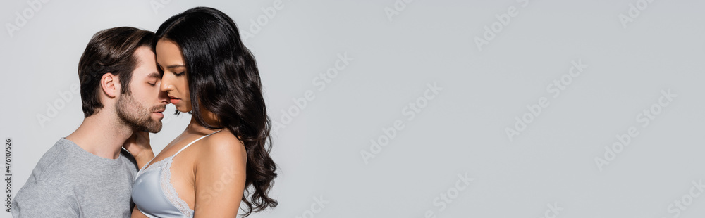 side view of passionate woman in bra near man with closed eyes isolated on grey, banner. side view of passionate woman in bra near man with closed eyes isolated on grey, banner.