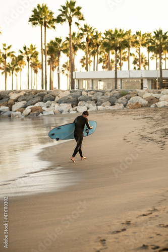 Canvas Print View of a man with a surfing board on the beach with palms trees at sunset