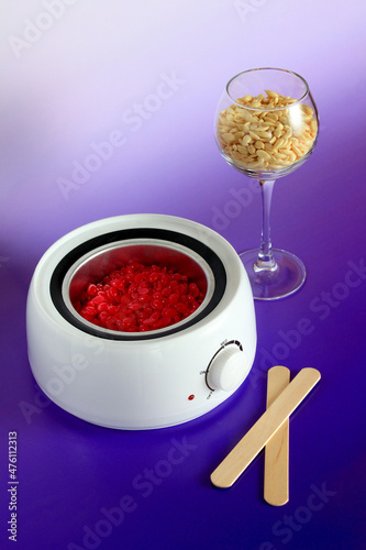 Electric wax heater, hot depilation wax granules in glass and wooden spatulas. beauty industry, body care, beauty business