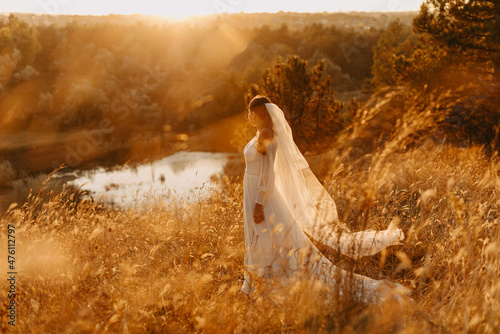Photo of dreamy bride in a lush dress whirls near the lake at sunset Fotobehang