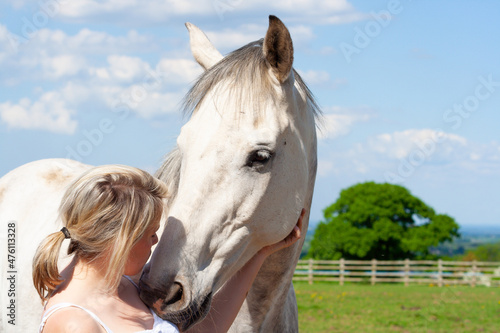Pretty young woman and her beautiful grey horse share an emotional loving moment in field on a sunny summers day in rural Shropshire.