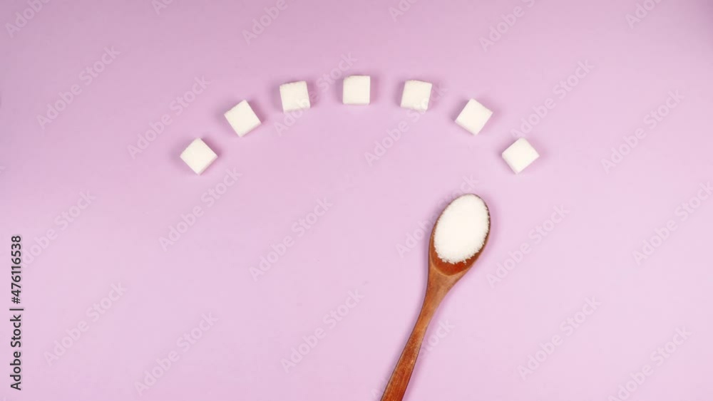 Diabetic blood sugar scale made of white sugar cubes and wooden eco spoon rolls over pink background