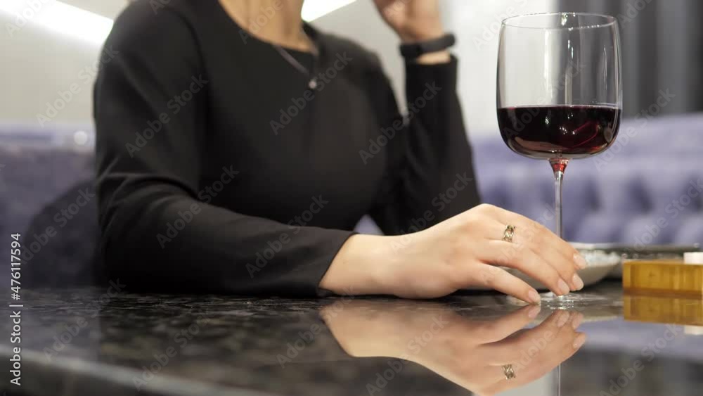 Reflection of a glass of red wine on the marble table of an elite restaurant. The girl's hand circles the stem of the glass in close-up. A girl in an evening dress on a date Reflection of a glass of red wine on the marble table of an elite restaurant. The girl's hand circles the stem of the glass in close-up. A girl in an evening dress on a date