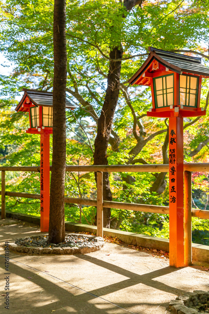 Naklejka premium traditional red lanterns lined up in front of the fence surrounded by autumn trees in shinto shrine