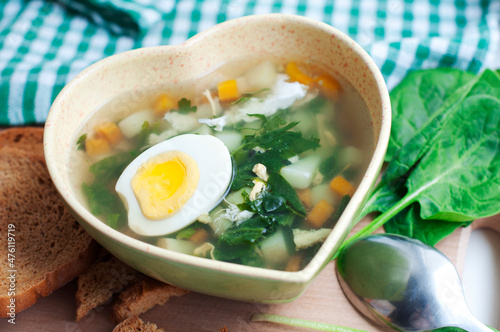 Green borsch with sorrel, parsley, egg and grens in the bowl form of heart with spoon on wooden background photo