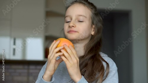 Little girl with long hair is licking a half of the orange. Happy childhood, healthy eating