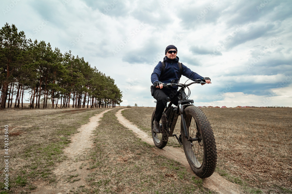 A man rides through the countryside on an electric bike with thick wheels. Sports hobby.