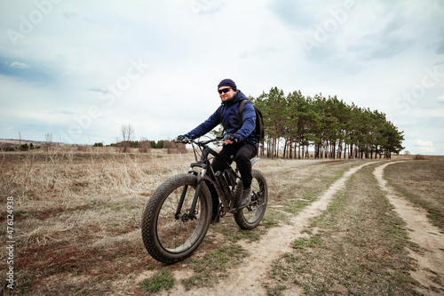 Fototapeta Naklejka Na Ścianę i Meble -  A man rides a fat bike on the road. Rural area.
