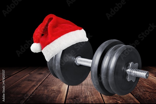 Fototapeta Naklejka Na Ścianę i Meble -  Heavy dumbbells weight plates with red Santa Claus hat. Healthy fitness lifestyle Christmas concept.
