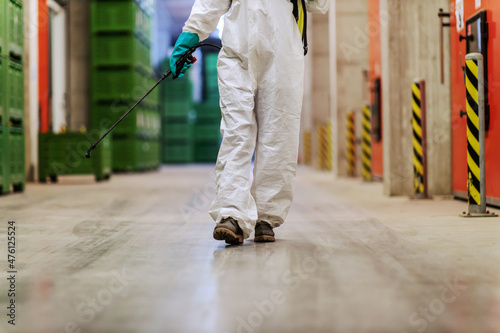COVID-19 danger alert stop spreading a virus. Professional in a protective suit walking throw a hallway and prevents the spread of the infection in the factory. Coronavirus defense Warning for COVID19